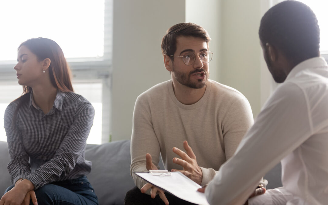 Young dissatisfied woman looks away while husband talking with mediator