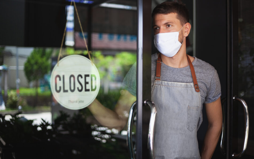 Man in safety mask hanging up sign closed on restaurant door